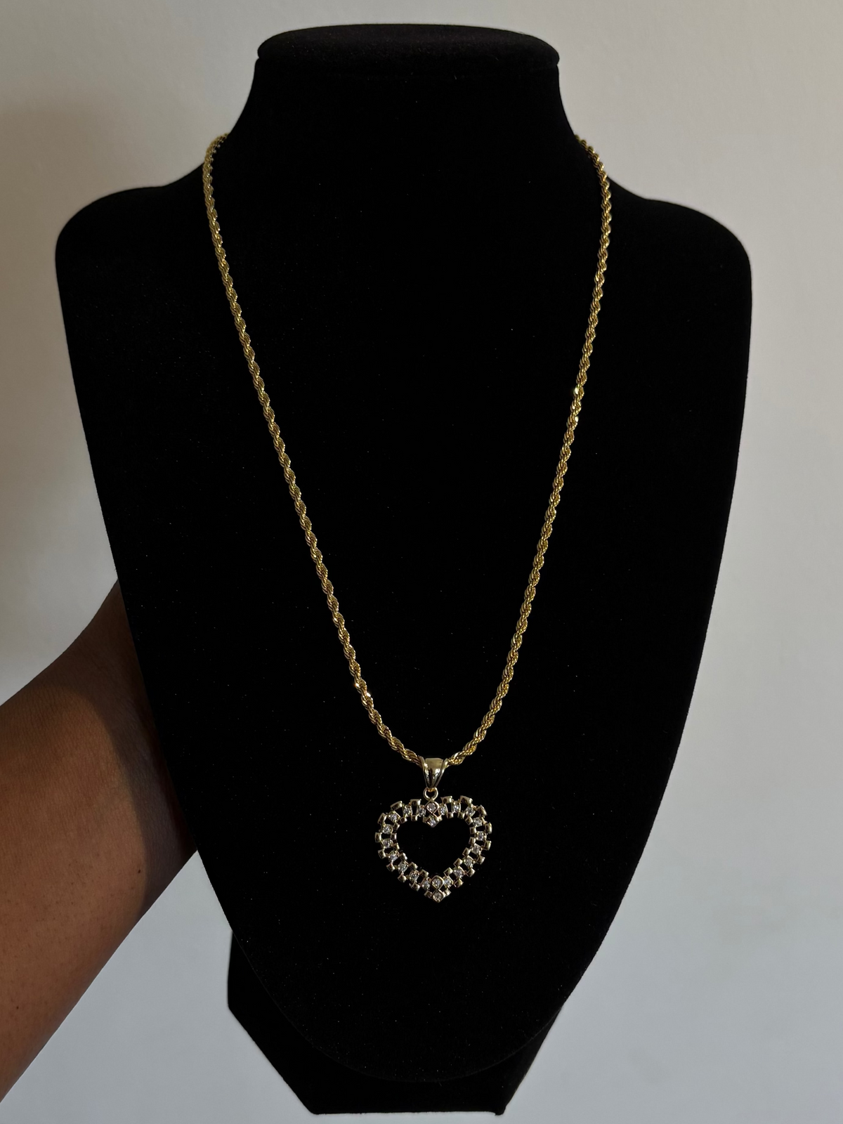 Gold necklace with a heart pendant on a black mannequin bust against a plain background 